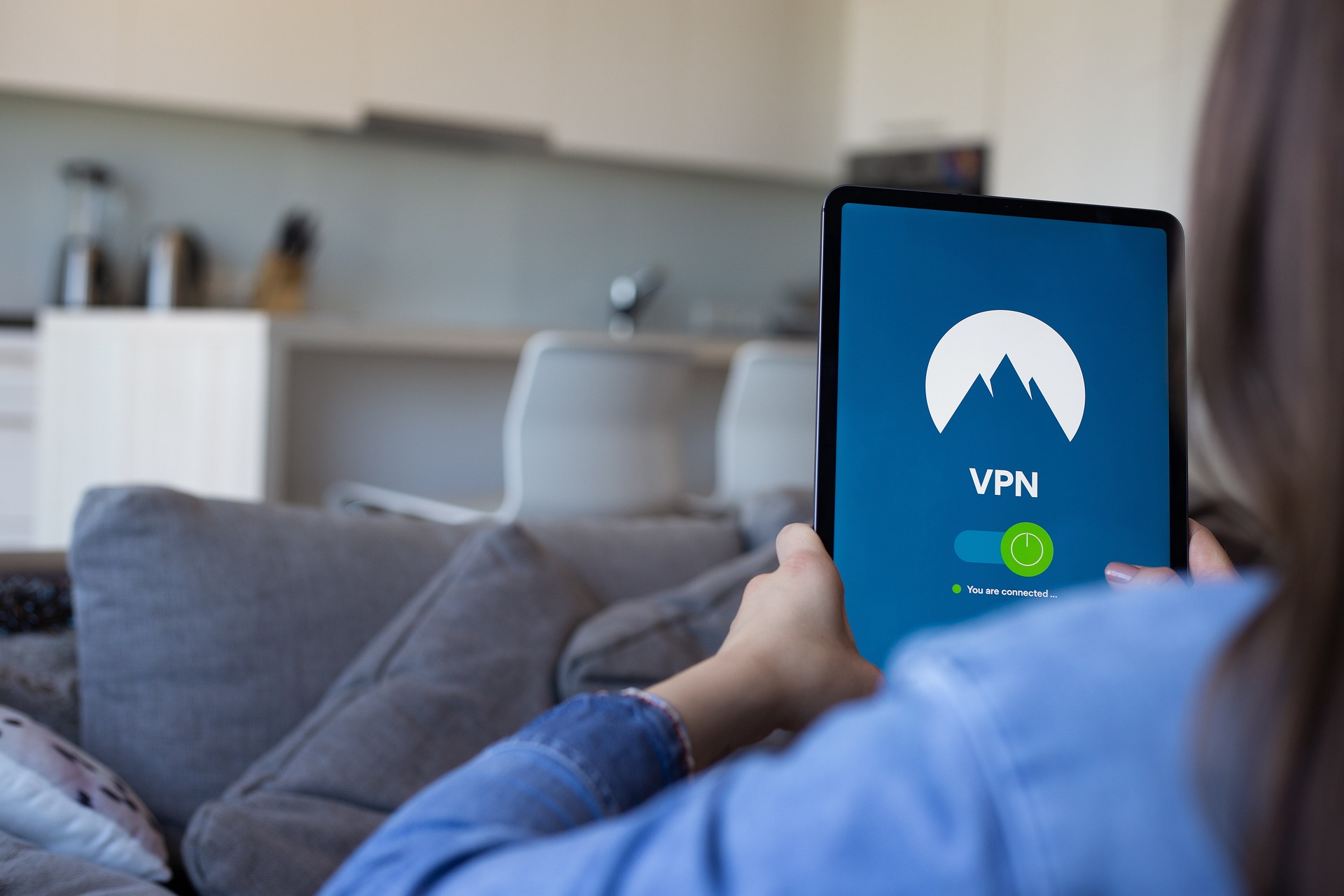 Wahrscheinlich eine Frau liegt auf dem Sofa mit einem Tablet in den Händen. Auf dem Tablet ist eine VPN-App mit aktivem Tunnel geöffnet.
