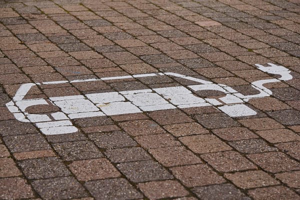 Bild lässt auf einen Parkplatz schließen. Auf den Pflastersteinen ist das Symbol für private batterieelektrische Fahrzeuge zu